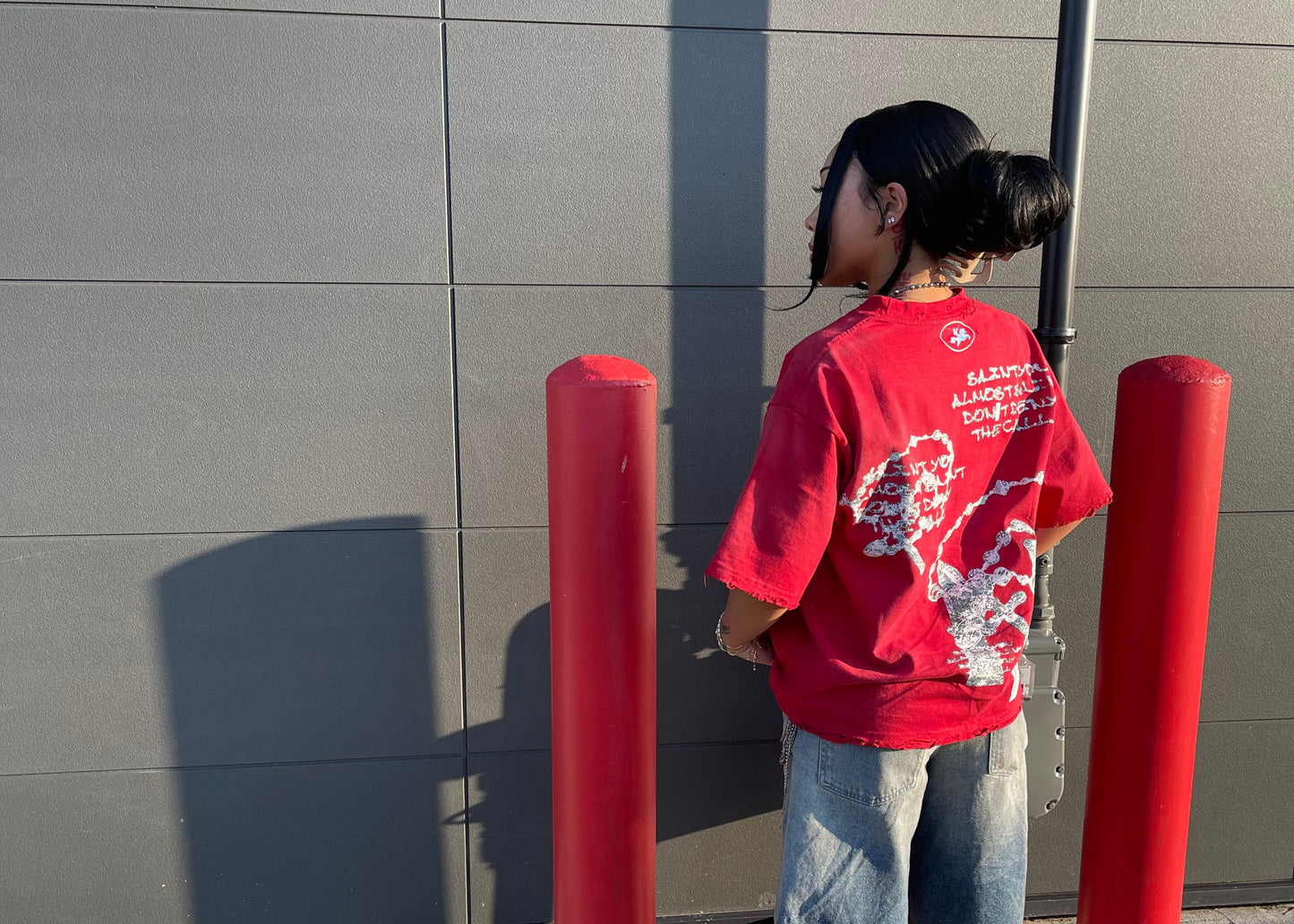 Person wearing a red sweatshirt and blue jeans standing on a tiled floor with red cylindrical objects.